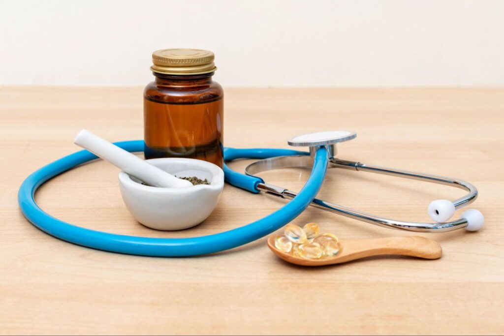 A stethoscope placed beside a mortar and pestle filled with herbal medicine, symbolizing the integration of conventional and holistic approaches to healthcare on a wooden background.