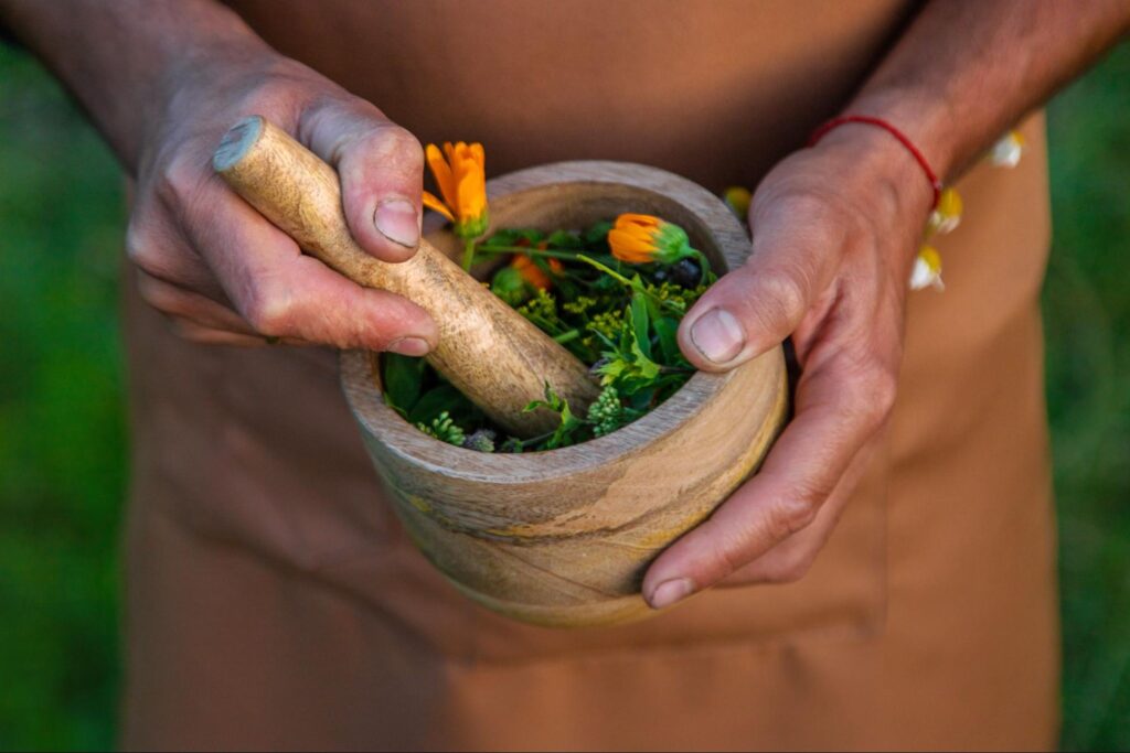 A close-up shot of a man's hands holding a mortal and pestle containing different medicinal herbs.