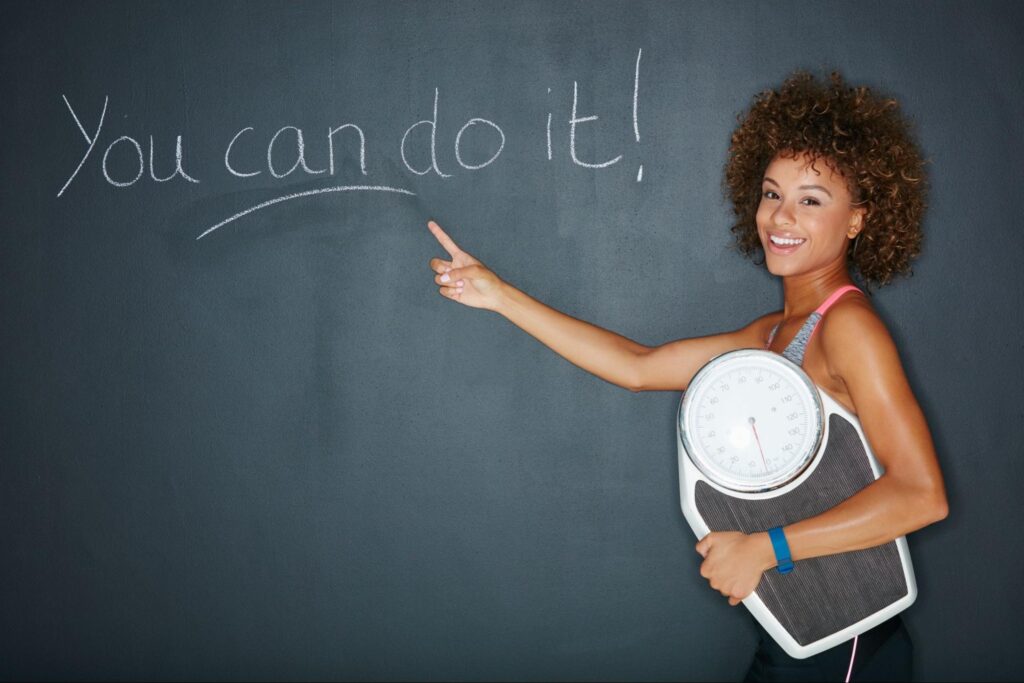 Woman holding a scale and pointing to the words “you can do it.”